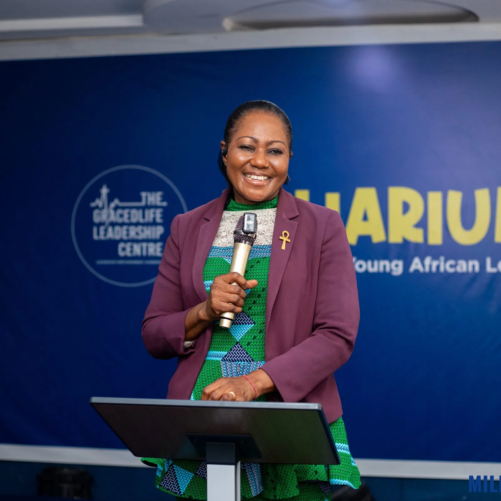 Rev. (Mrs.) Angela Carmen Appiah speaks at the lectern in front of the Miliarium banner